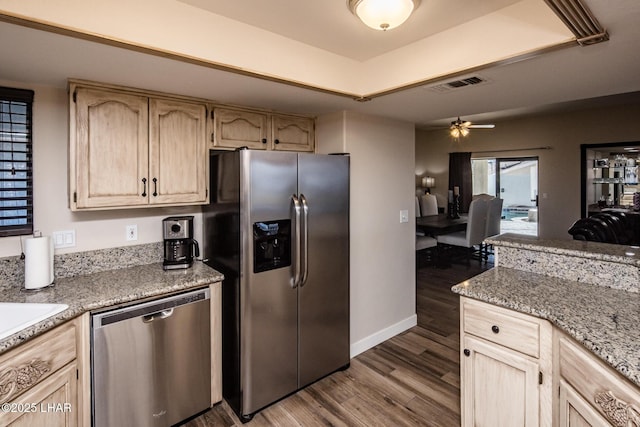 kitchen featuring dark hardwood / wood-style flooring, stainless steel appliances, a tray ceiling, light stone countertops, and light brown cabinetry