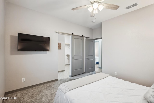 carpeted bedroom featuring visible vents, a walk in closet, a barn door, baseboards, and ceiling fan