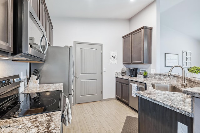 kitchen with light wood-style flooring, a sink, light stone counters, stainless steel appliances, and dark brown cabinetry