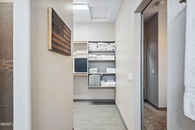 corridor featuring attic access, baseboards, and wood finished floors