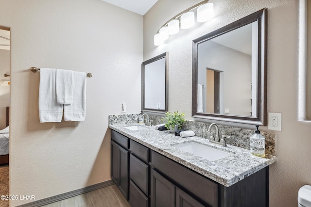 ensuite bathroom with double vanity, connected bathroom, wood finished floors, and a sink