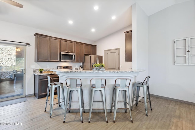 kitchen featuring light stone countertops, a kitchen bar, lofted ceiling, light wood-style flooring, and appliances with stainless steel finishes