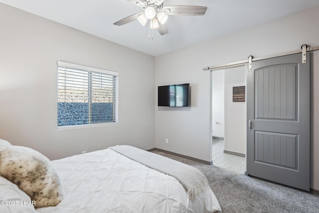 carpeted bedroom with a barn door, a ceiling fan, and baseboards