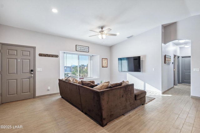 living area featuring baseboards, visible vents, light wood-style flooring, arched walkways, and ceiling fan