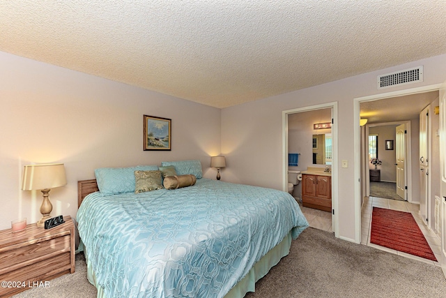 carpeted bedroom featuring ensuite bathroom and a textured ceiling