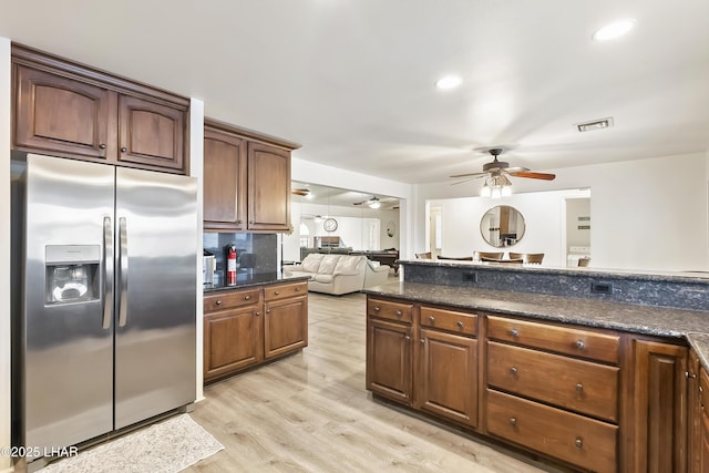 kitchen featuring dark stone countertops, light wood-type flooring, stainless steel fridge, ceiling fan, and decorative backsplash