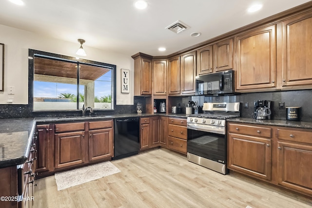 kitchen featuring sink, tasteful backsplash, light wood-type flooring, dark stone counters, and black appliances