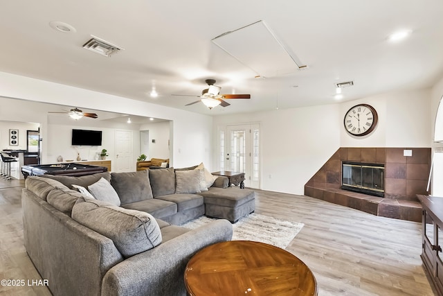 living room featuring ceiling fan, a tiled fireplace, and light hardwood / wood-style flooring