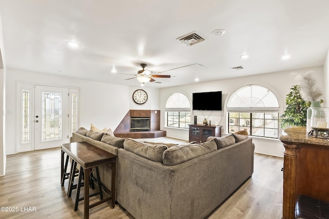 living room with ceiling fan, a tile fireplace, and light wood-type flooring