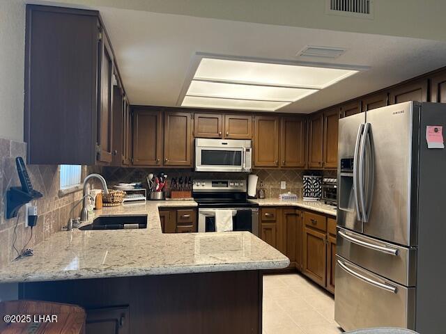 kitchen with sink, stainless steel appliances, tasteful backsplash, light stone countertops, and kitchen peninsula