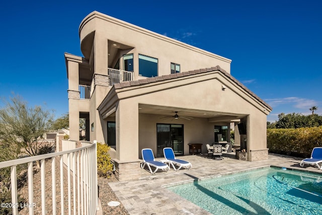 back of house with an outdoor pool, a patio, a balcony, ceiling fan, and stucco siding