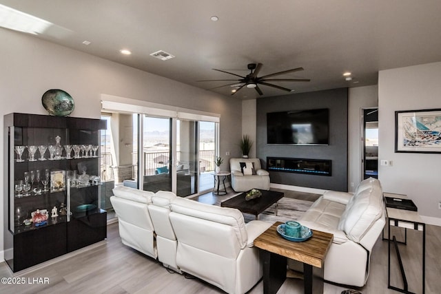 living area featuring baseboards, a ceiling fan, a glass covered fireplace, light wood-type flooring, and recessed lighting