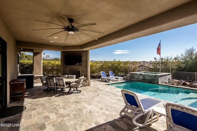 view of swimming pool with an outdoor stone fireplace, a patio area, fence, and a ceiling fan