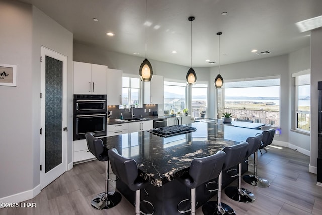 kitchen featuring a breakfast bar area, dobule oven black, white cabinetry, stainless steel dishwasher, and a center island