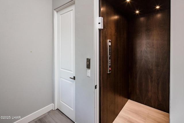 hall featuring baseboards, wood finished floors, and elevator