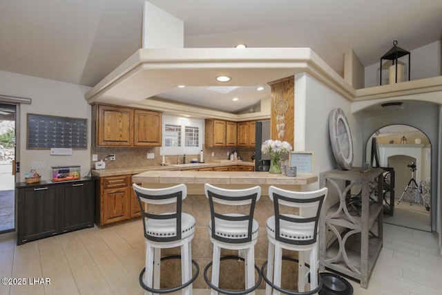 kitchen with vaulted ceiling, light countertops, brown cabinets, tasteful backsplash, and a kitchen bar