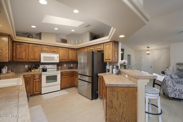 kitchen with white appliances, brown cabinets, a kitchen breakfast bar, a peninsula, and a sink