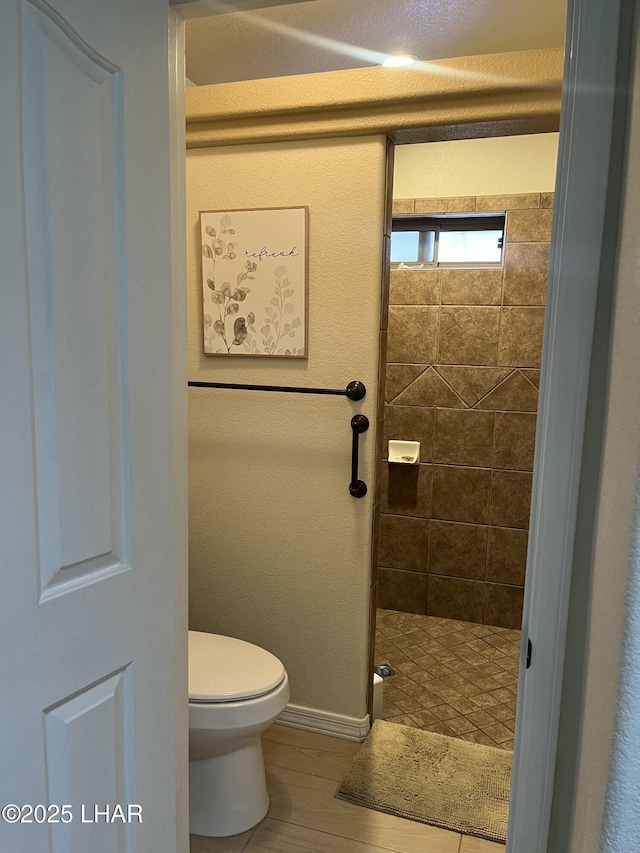 bathroom with wood finished floors, a tile shower, toilet, and baseboards