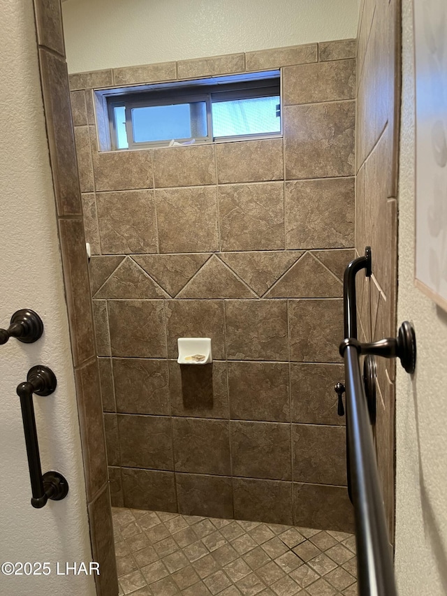 bathroom with a textured wall and a tile shower