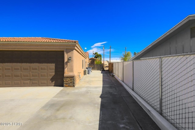 view of property exterior featuring a garage, fence, a tiled roof, concrete driveway, and stone siding