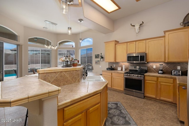 kitchen featuring tasteful backsplash, light brown cabinets, stainless steel appliances, pendant lighting, and a sink