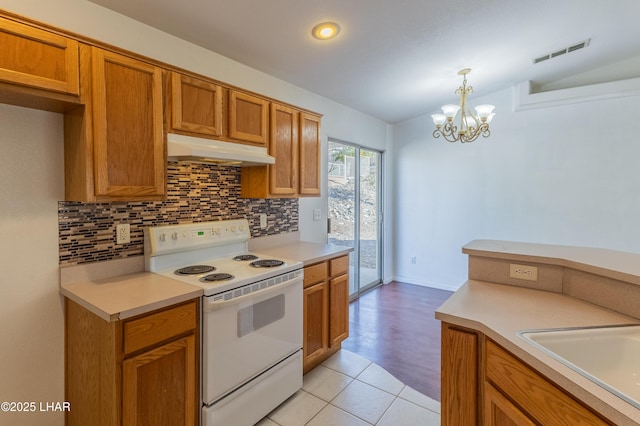 kitchen featuring visible vents, under cabinet range hood, white electric range, backsplash, and light countertops