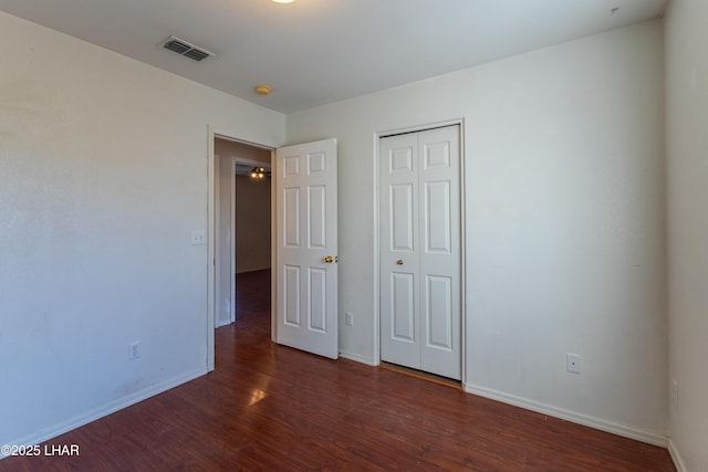 unfurnished bedroom with visible vents, wood finished floors, baseboards, and a closet