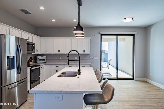 kitchen featuring sink, appliances with stainless steel finishes, white cabinetry, a center island with sink, and decorative light fixtures