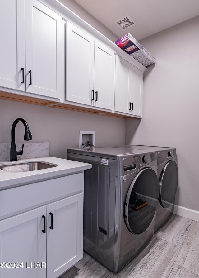 laundry room with cabinets, washer and dryer, sink, and light wood-type flooring