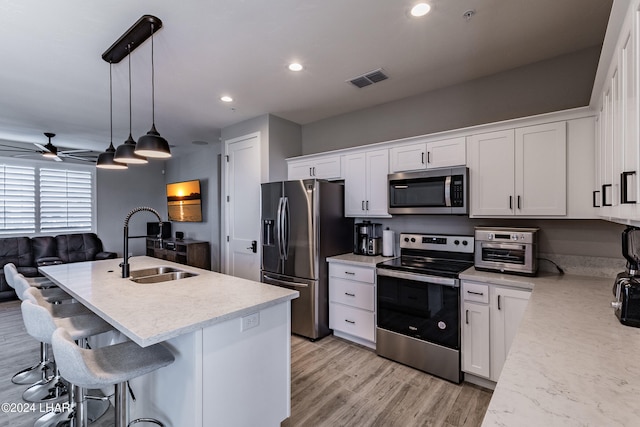 kitchen featuring sink, white cabinetry, decorative light fixtures, a center island with sink, and appliances with stainless steel finishes