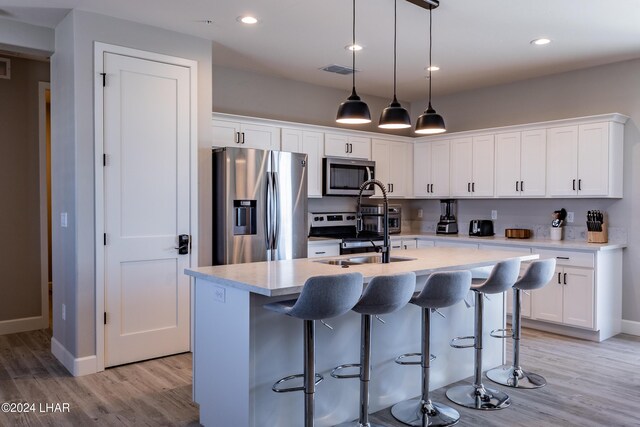 kitchen with stainless steel appliances, white cabinetry, sink, and an island with sink