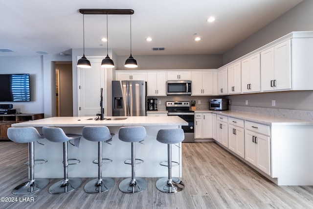 kitchen with sink, white cabinetry, appliances with stainless steel finishes, pendant lighting, and a kitchen island with sink