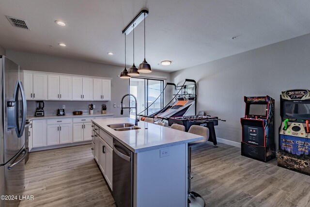 kitchen with sink, white cabinetry, stainless steel fridge, dishwashing machine, and a kitchen island with sink