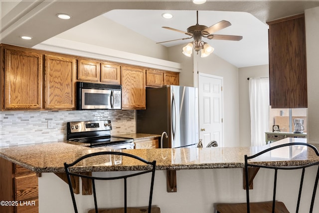 kitchen with decorative backsplash, stone countertops, brown cabinets, and stainless steel appliances