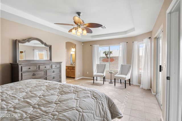 bedroom with visible vents, baseboards, a tray ceiling, light tile patterned flooring, and arched walkways