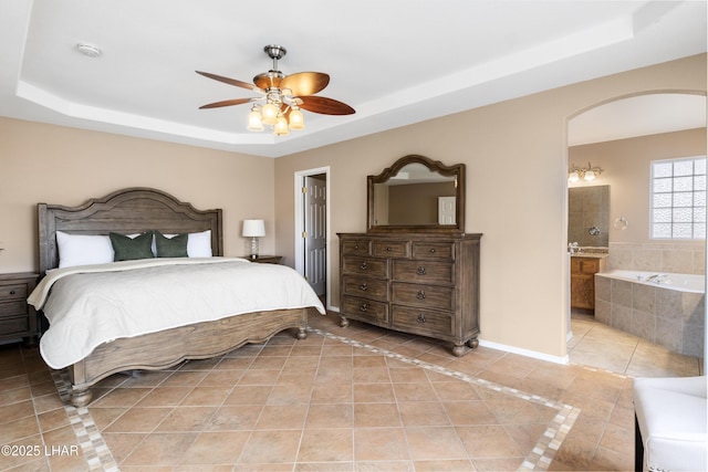 bedroom featuring light tile patterned floors, connected bathroom, arched walkways, and a tray ceiling