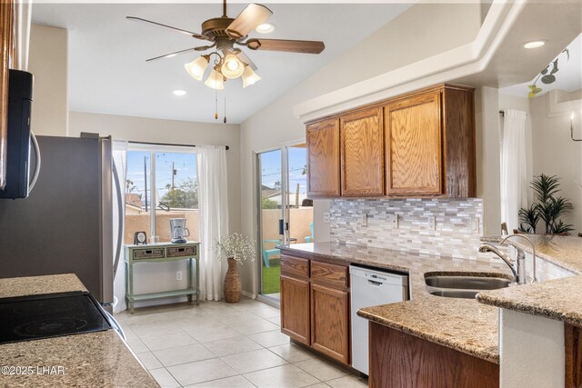 kitchen featuring tasteful backsplash, lofted ceiling, light stone counters, appliances with stainless steel finishes, and a sink