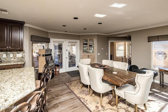 dining area with ornamental molding, a healthy amount of sunlight, light wood-type flooring, and french doors