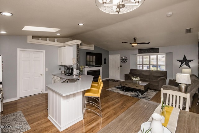 kitchen with white cabinetry, hardwood / wood-style flooring, a breakfast bar area, sink, and vaulted ceiling with skylight