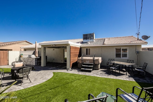 back of house featuring a lawn, a patio area, a hot tub, and exterior kitchen