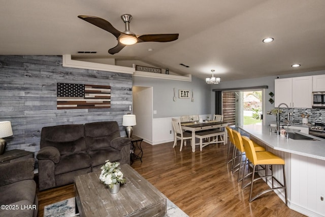 living room with vaulted ceiling, sink, wood walls, ceiling fan with notable chandelier, and dark wood-type flooring