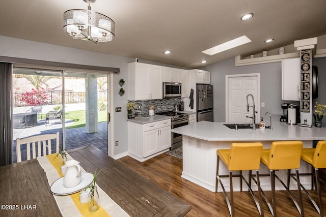 kitchen with a breakfast bar area, sink, appliances with stainless steel finishes, white cabinets, and vaulted ceiling with skylight