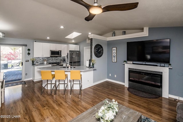 kitchen featuring stainless steel appliances, dark wood-type flooring, white cabinets, a kitchen breakfast bar, and decorative backsplash