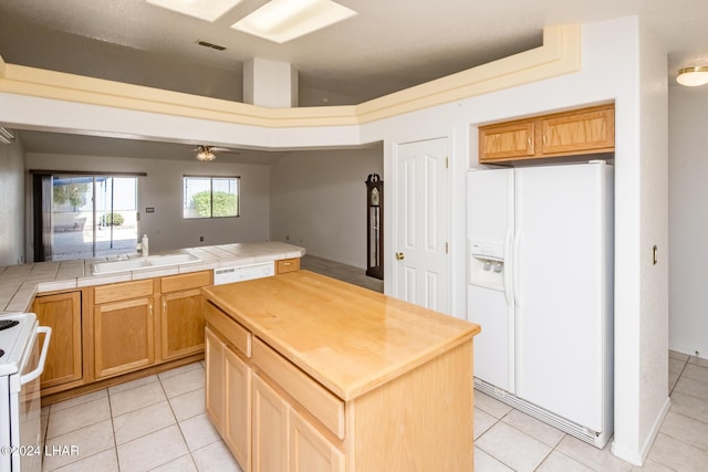 kitchen with sink, white appliances, a kitchen island, tile counters, and light tile patterned flooring