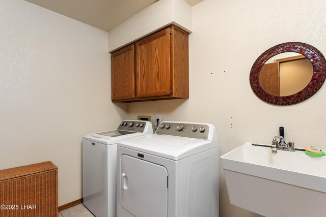 laundry room with cabinet space, light tile patterned floors, washing machine and dryer, and a sink