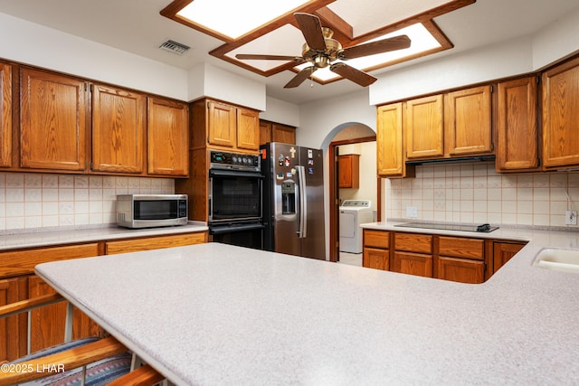 kitchen with visible vents, black appliances, light countertops, decorative backsplash, and washer / dryer