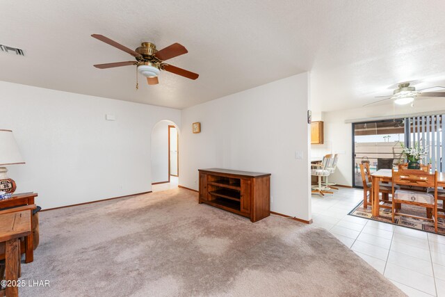 living area with arched walkways, visible vents, light carpet, and a ceiling fan