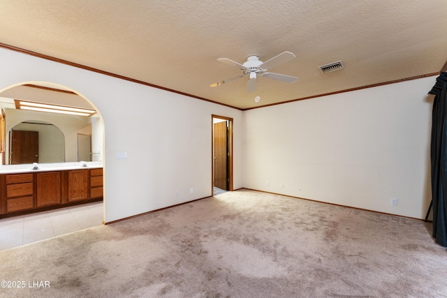 unfurnished bedroom with visible vents, ornamental molding, a textured ceiling, arched walkways, and light colored carpet