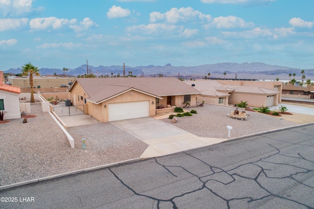 view of front of house with stucco siding, a gate, fence, a mountain view, and concrete driveway