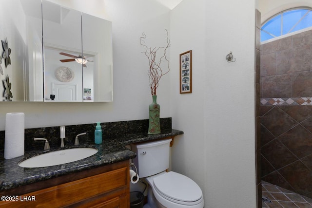 bathroom featuring toilet, tiled shower, vanity, and a ceiling fan